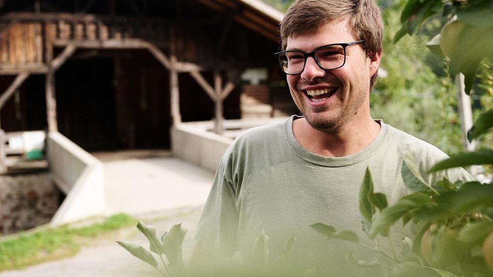 Apple farmer standing by an apple tree in front of the barn