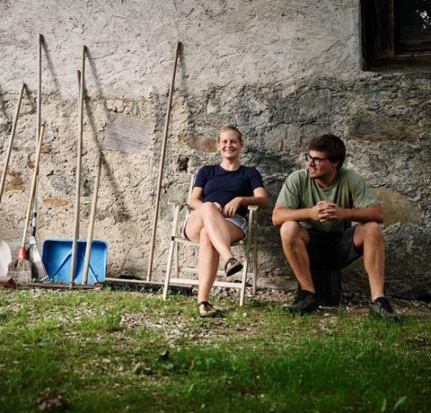 Apple farmer woman and man sitting by stone wall with farm tools