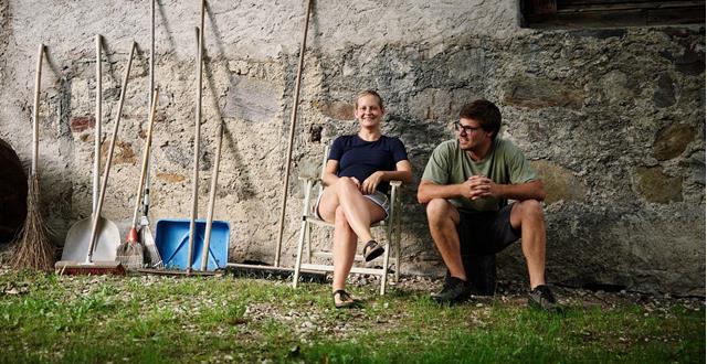 Apple farmer woman and man sitting by stone wall with farm tools