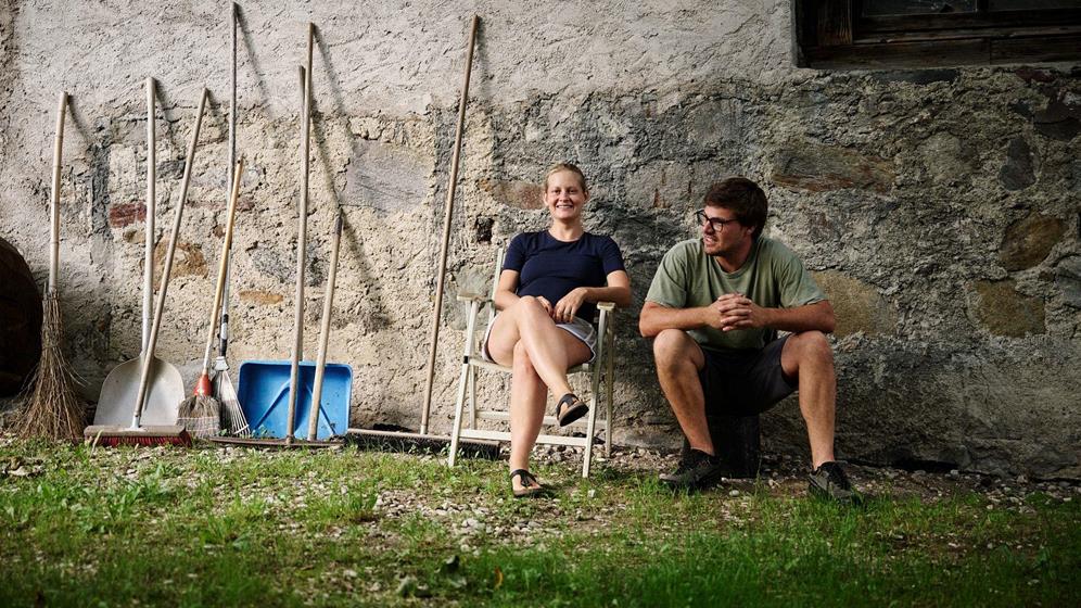 Apple farmer woman and man sitting by stone wall with farm tools